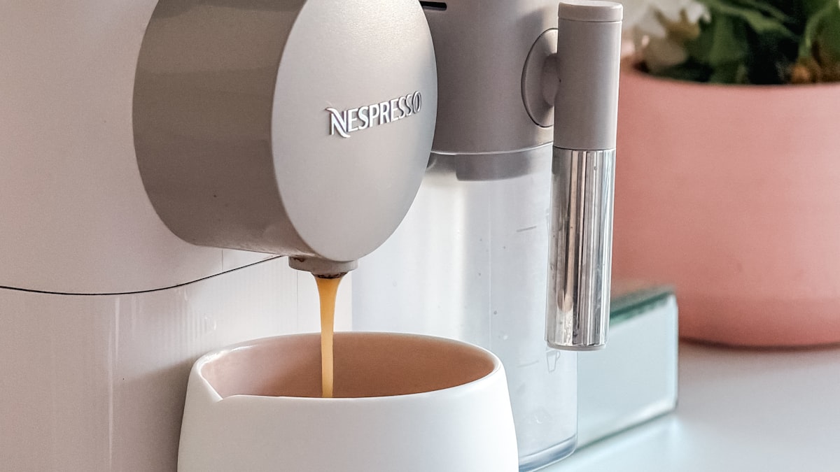 Nespresso capsule coffee machine pouring espresso into a white cup