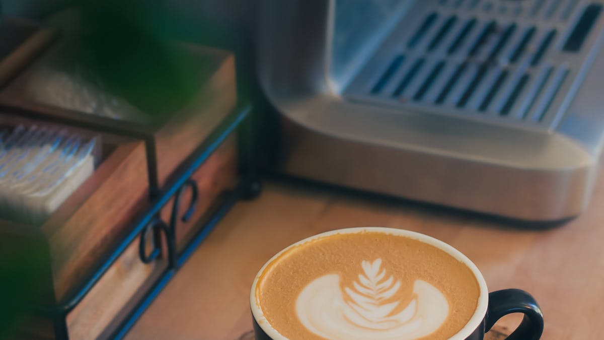 Flat white with latte art in a black cup beside a home espresso machine